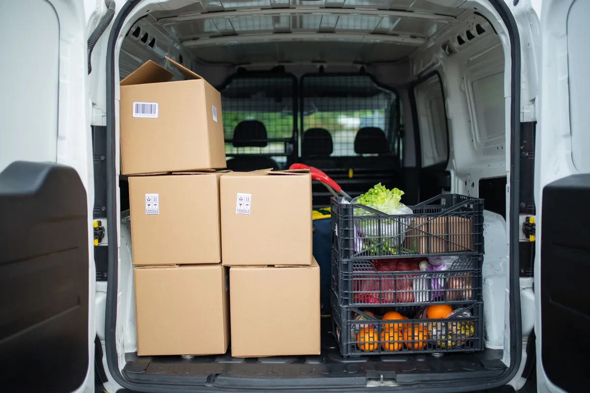 Gestapelte Kartons und eine Transportkiste im offenen Laderaum eines weißen Transporters