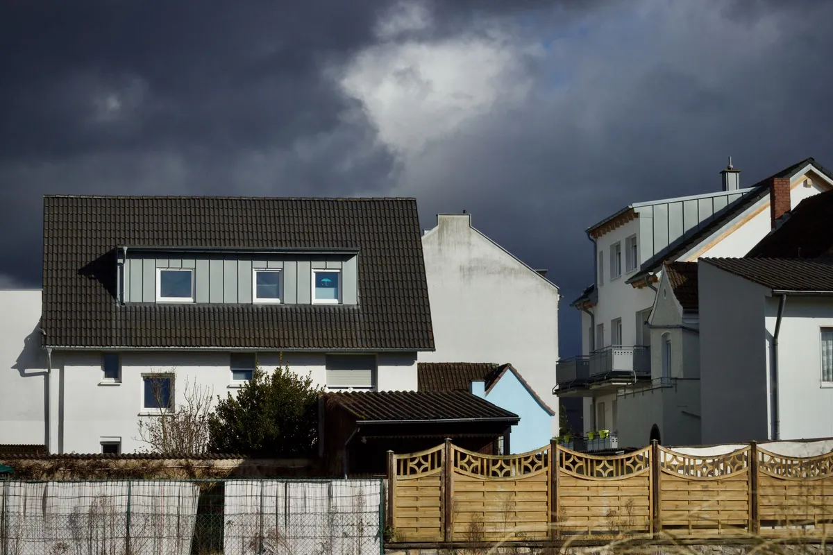 Wohnhäuser mit Satteldach und Holzzaun unter dunklen Wolken in einem Wohngebiet