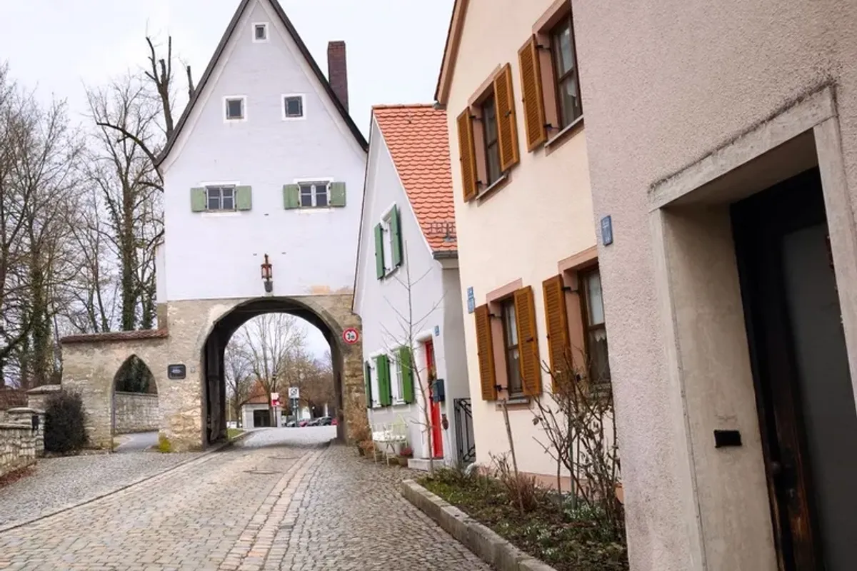 Gepflasterte Altstadtgasse mit altem Torturm und hellen Giebelhäusern an grauem Wintertag