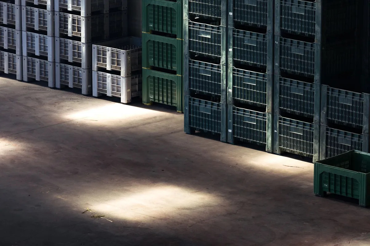Gestapelte Kunststoffboxen in einer Lagerhalle, Sonnenlicht fällt schräg auf den Betonboden