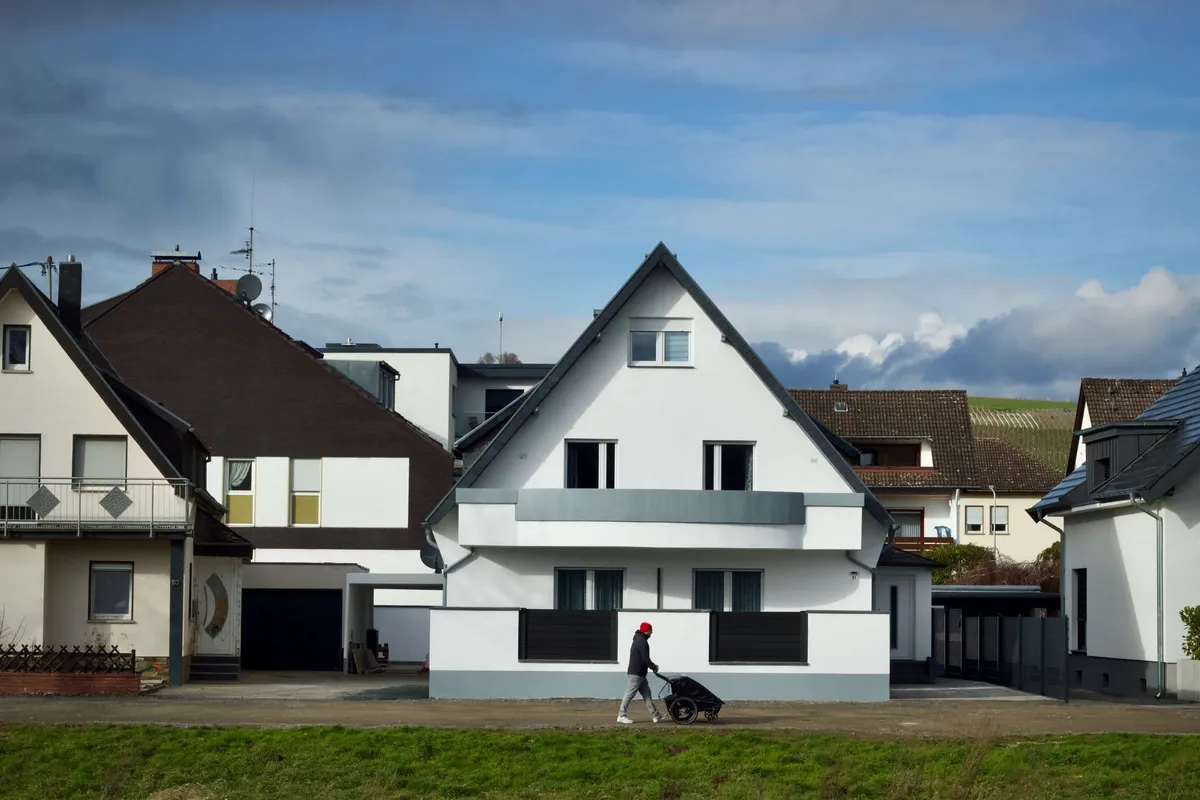 Weißes Einfamilienhaus mit Satteldach in einer Wohnsiedlung, Passant mit Handwagen davor