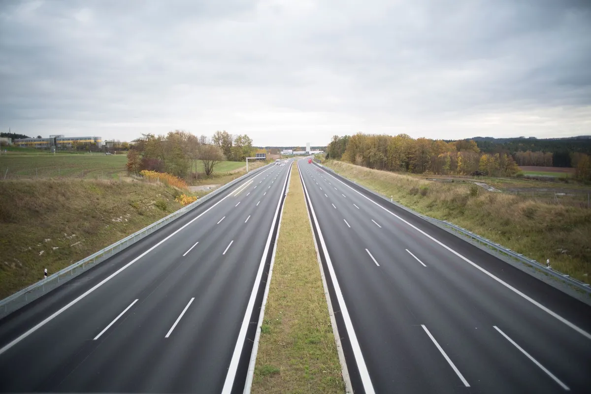 Leere Autobahn mit zwei Fahrbahnen und Grünstreifen an einem bewölkten Herbsttag