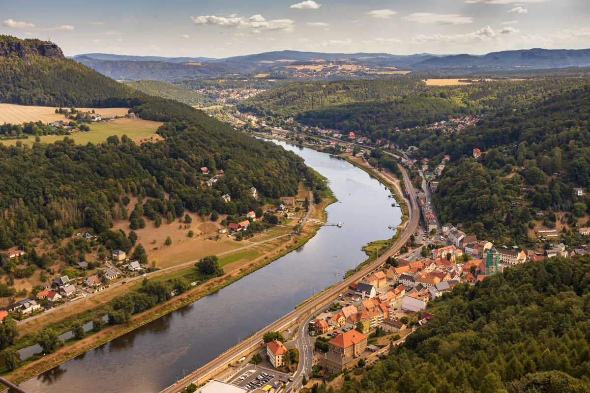 Luftbild eines Flusstals mit Ortschaft, Bahnlinie und bewaldeten Hügeln