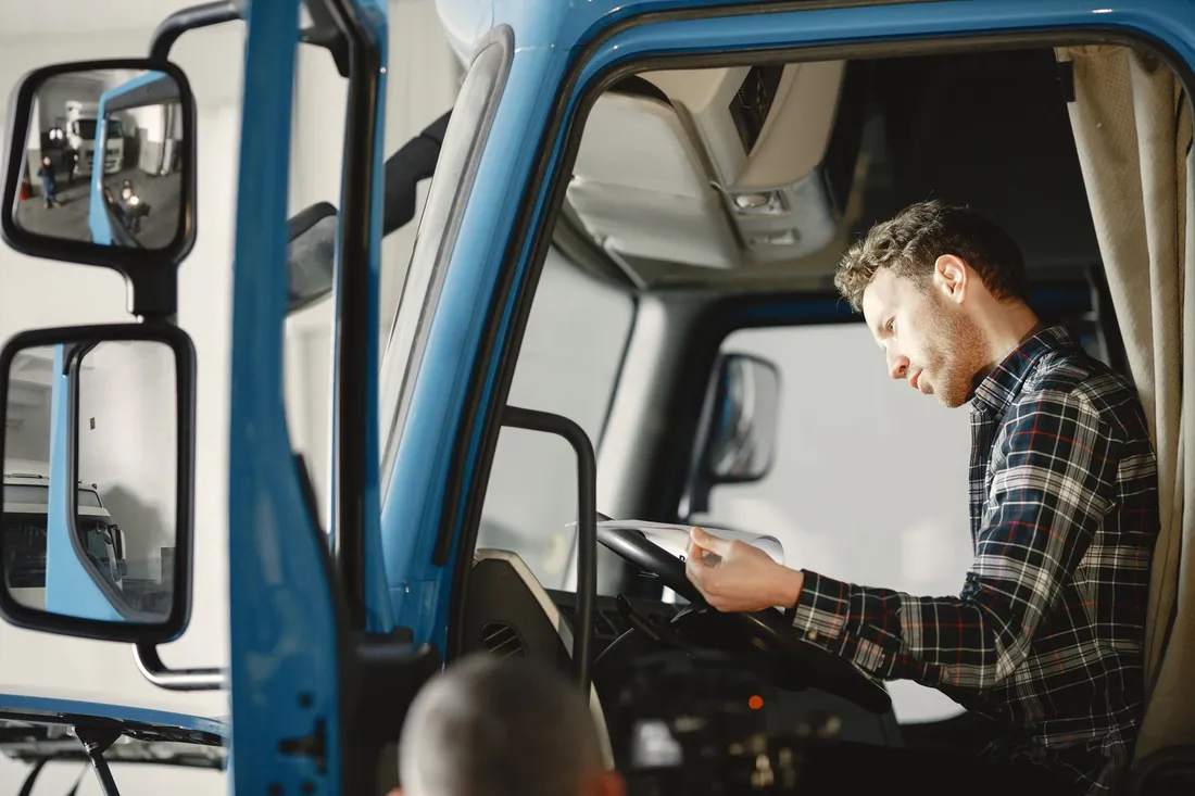 Fahrer sitzt im Führerhaus eines blauen Lkw und prüft seine Papiere